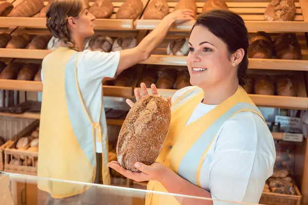 Verkäuferin in einer Bäckerei hält Brot in der Hand