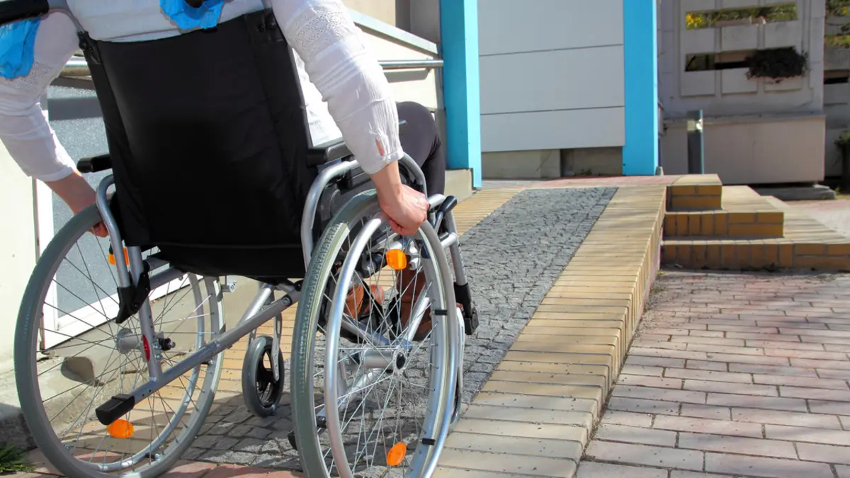 Rollstuhlfahrerin an Rampe vor Hauseingang