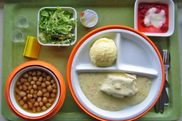 Ein Krankenhaustablett mit verschiedenen, portionierten Essensgängen drauf und zwei Gläsern Wasser.