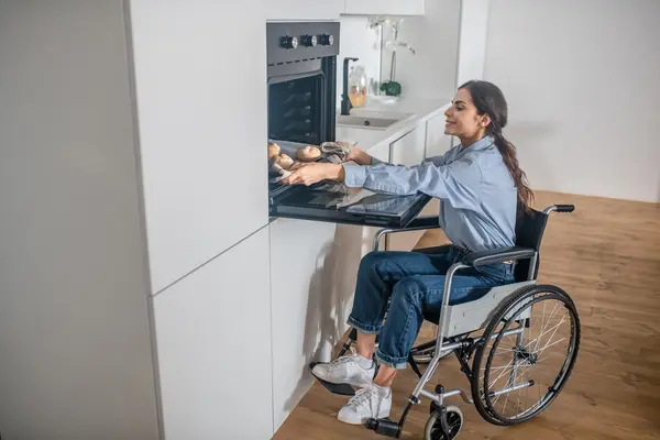 Eine Frau im Rollstuhl holt ein Backblech aus dem Backofen.