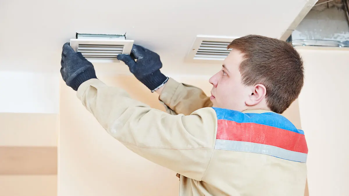 Installateur arbeitet an Lüftungsöffnung an einer Decke