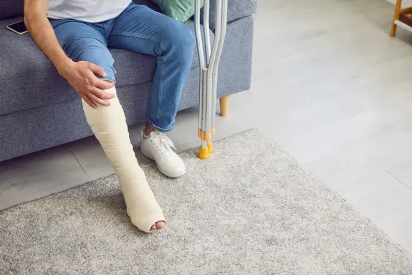 Mann sitzt auf Sofa mit verletztem Bein