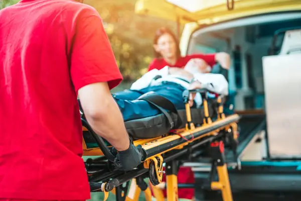 Zwei Sanitäter schieben eine Bare mit einem Patienten in einen Krankenwagen