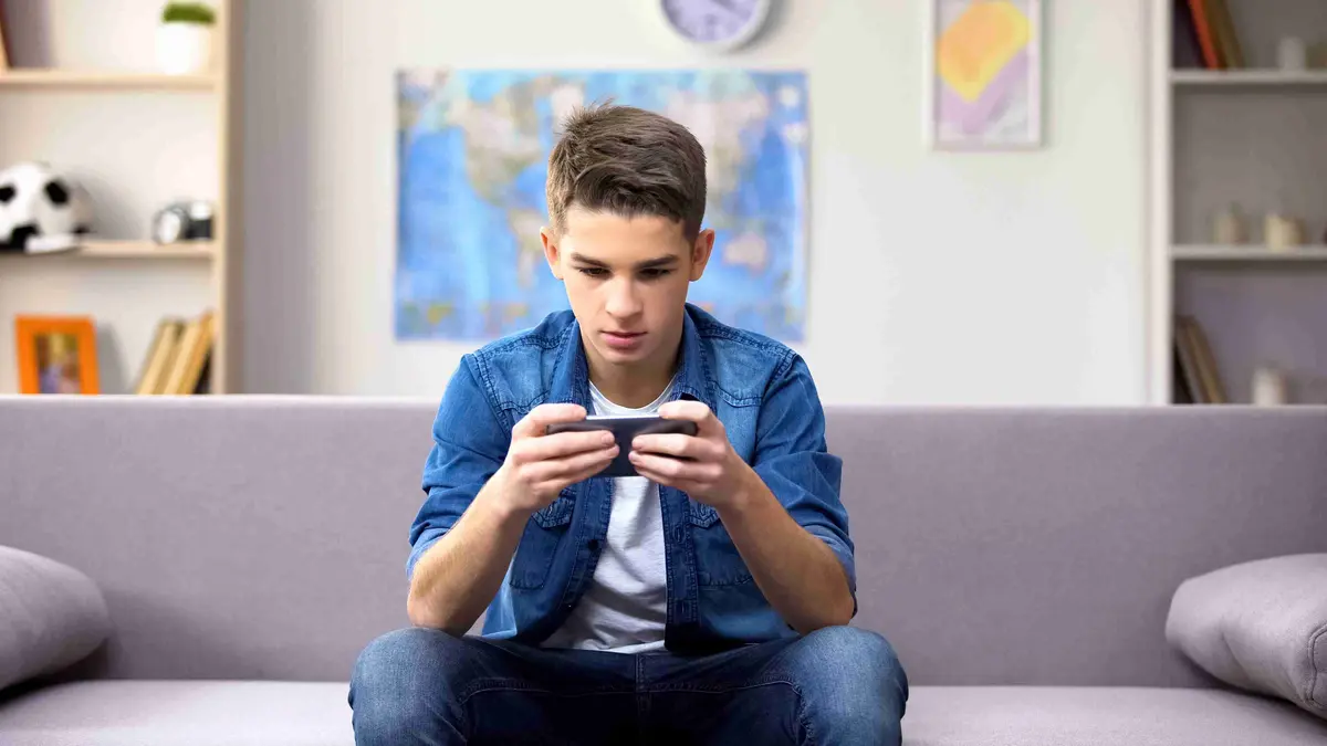 Junge sitzt auf Couch mit Handy in der Hand