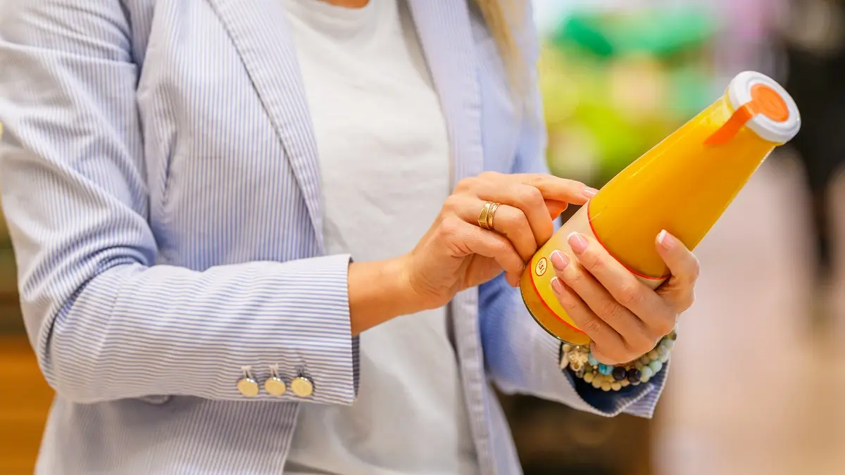 Frau im Supermarkt, die ein Etikett einer Saftflasche studiert.