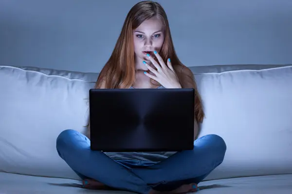 Junge Frau blickt erschrocken auf Laptop