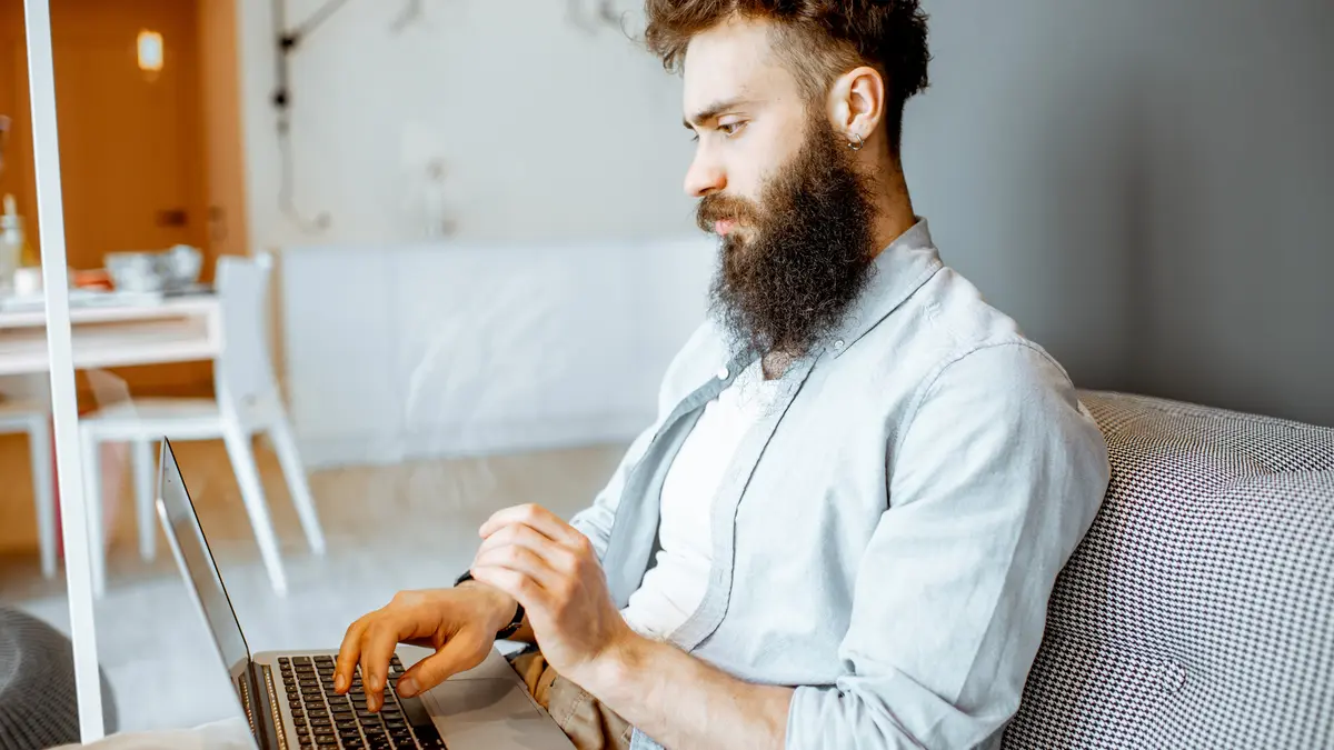 Junger Mann sitzt mit Laptop auf dem Sofa