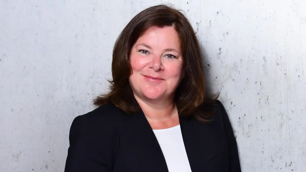 Eine Frau im Portrait vor einer hellen Wand. Sie lächelt in die Kamera.