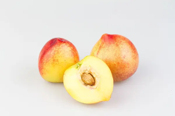 Zwei ganze und ein halber Pfirsich mit Kern auf einer weißen Fläche.