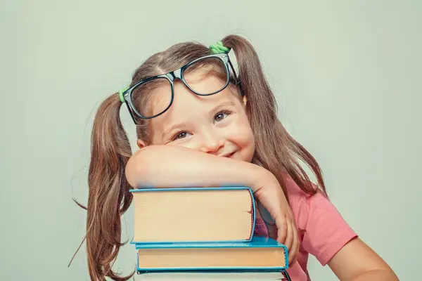 Mädchen mit Brille hat den Arm über einen Stapel Bücher gelegt.
