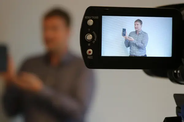 Ein Mann zeigt ein Smartphone in eine Videokamera.