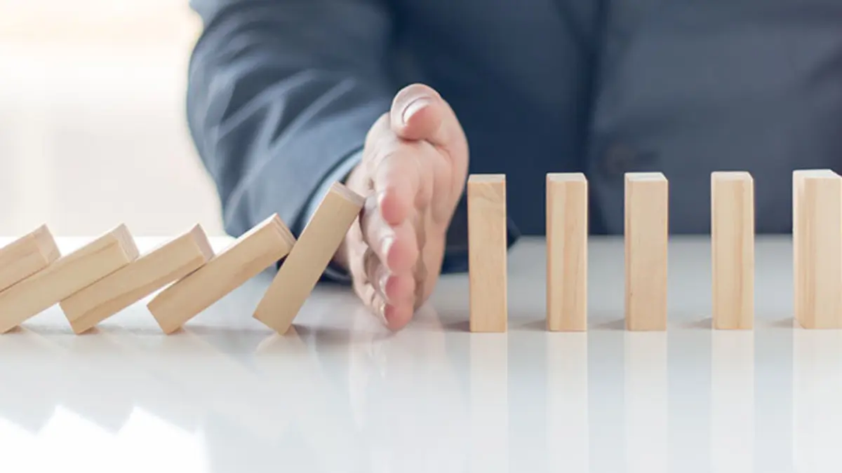 Eine Hand stoppt eine Reihe umkippender Dominosteine