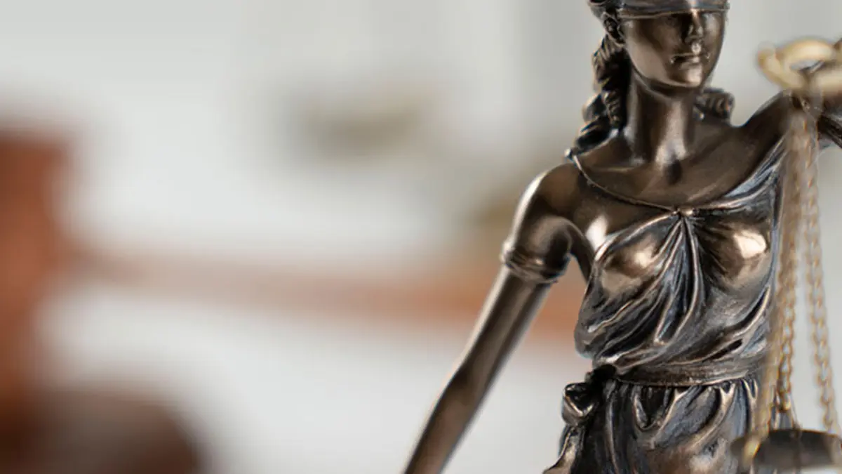 Eine Skulptur der Justitia auf einem Tisch, im Hintergrund der Hammer des Gerichts