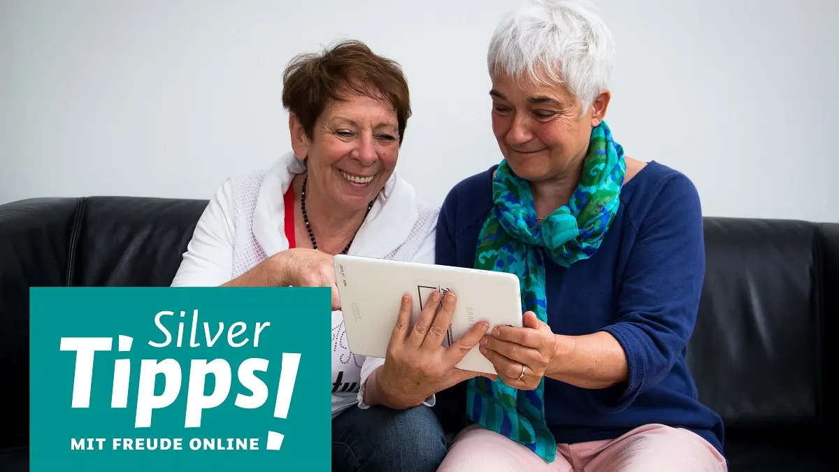Zwei ältere Frauen auf einem Sofa schauen auf ein Tablet.