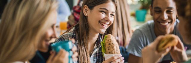 Eine Gruppe Jugendlicher isst und trinkt an einem Tisch in einer Mensa