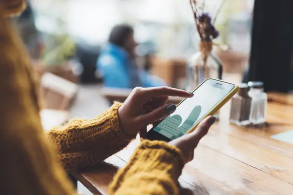 Eine Frau sitzt an einem Tisch und blickt auf ihr Smartphone.