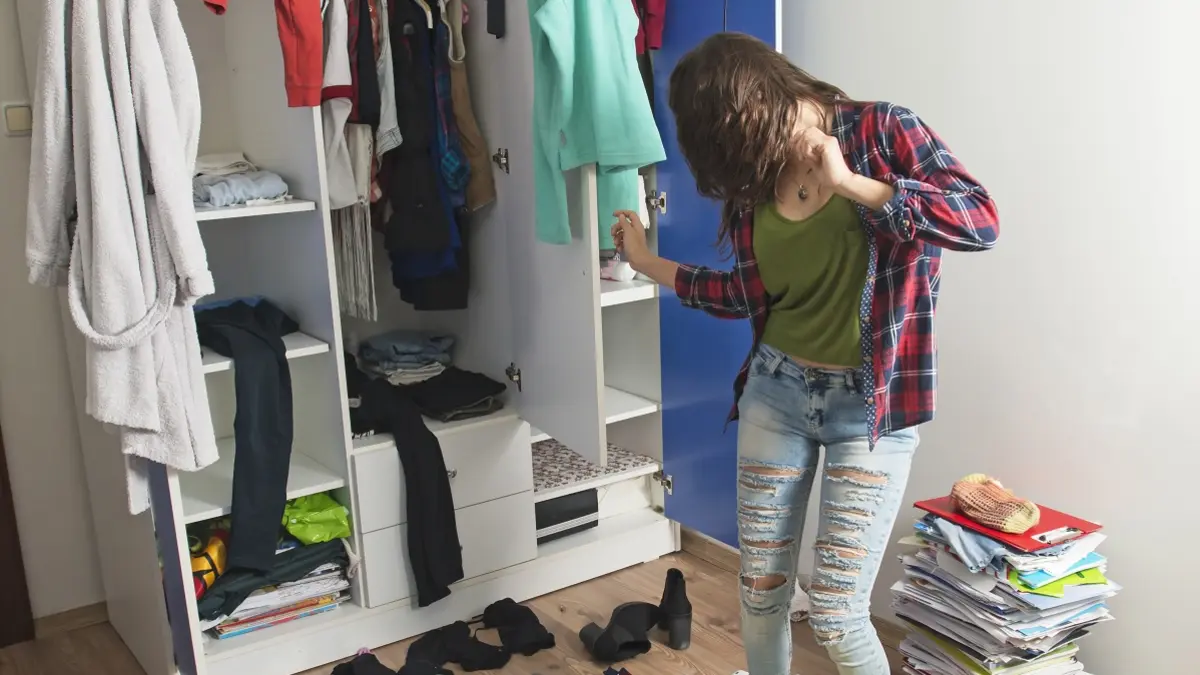 Junge Frau tanzt vor ihrem Kleiderschrank. Drumherum liegen lauter Kleidungsstücke.