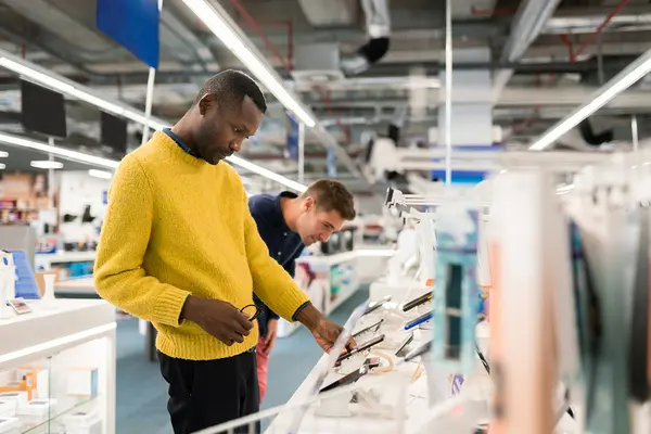 Zwei Männer begutachten Smartphones in einem Elektronikfachmarkt.