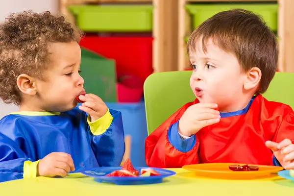 Zwei Kleinkinder mit Lätzchen essen Obst von Tellern