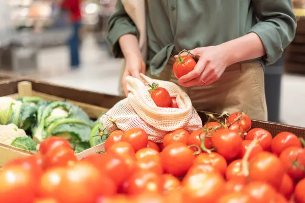 Eine Frau packt Tomaten in ein Stoffsäckchen.