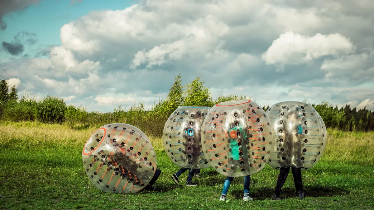 Jugendliche spielen auf einer Wiese in großen aufblasbaren Gummibällen (Bumperballs)  
