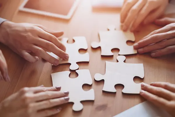 Mehrere Händepaare legen auf einem Tisch vier große Holz-Puzzleteile zusammen