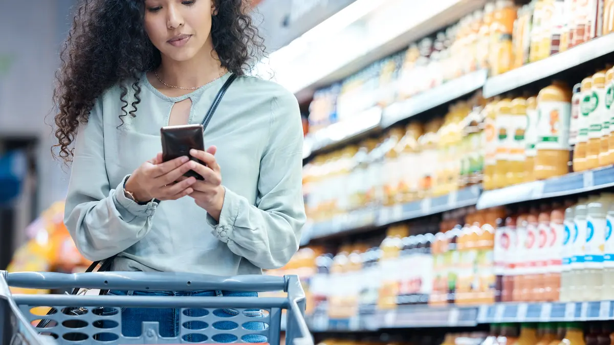 Eine Frau nutze eine Supermarkt-App auf ihrem Handy beim Einkaufen