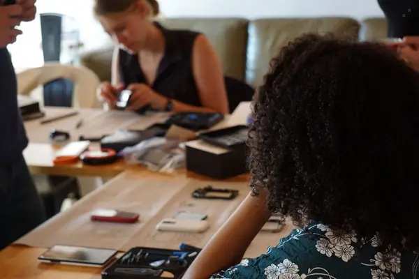 Menschen sitzen an einem Tisch und reparieren Smartphones und andere elektronische Geräte
