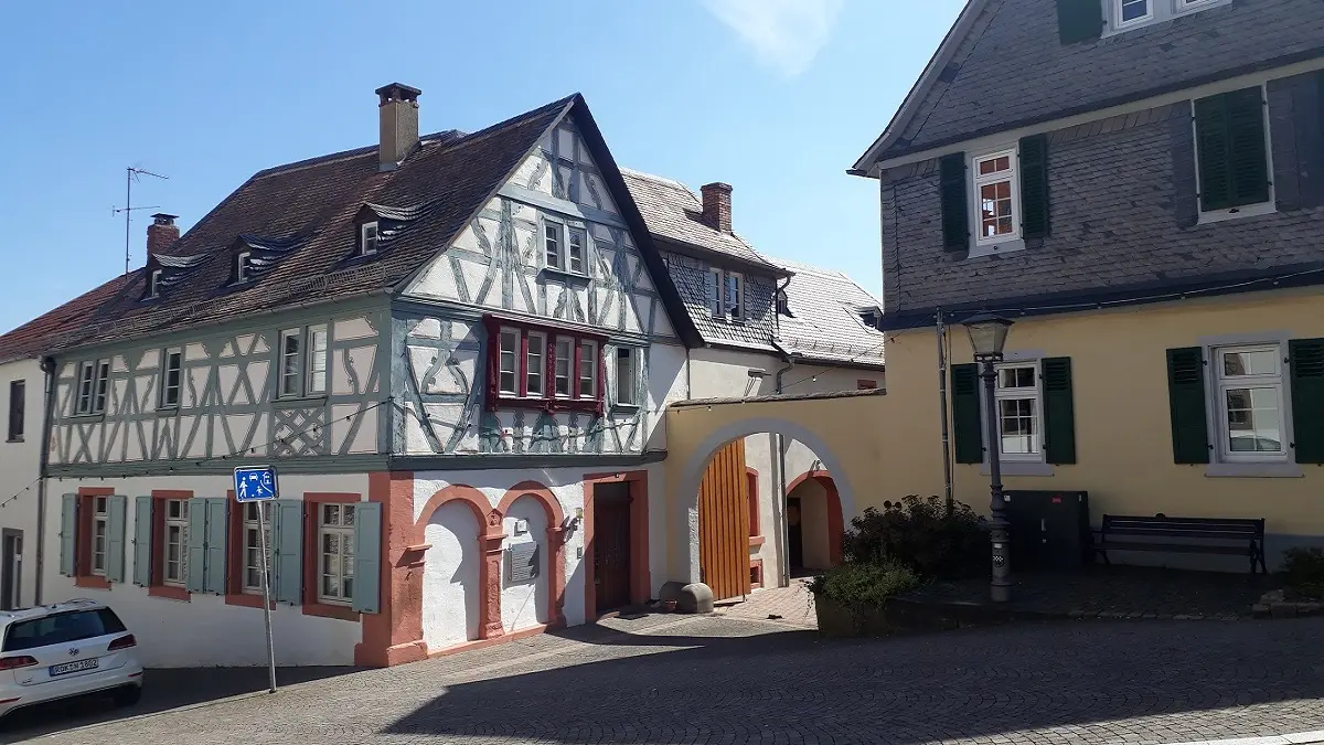 Zwei ältere Häuser an einer gepflasterten Straße.
