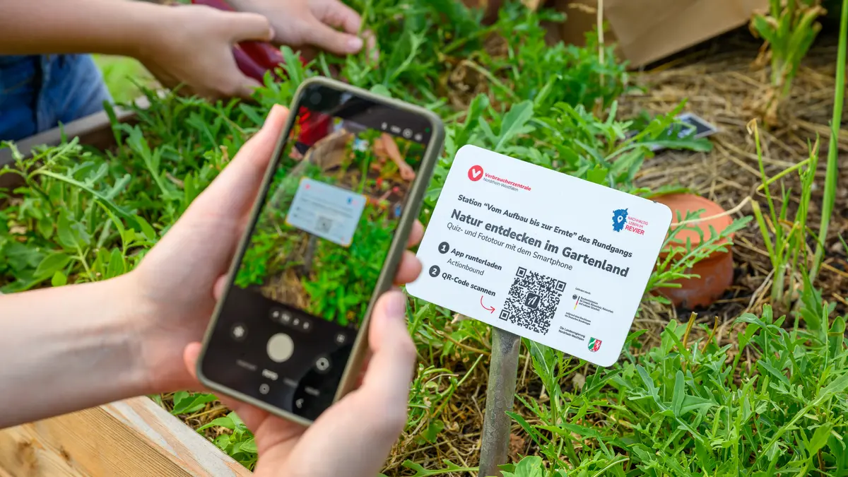 Eine Hand mit Smartphone scannt einen QR-Code von einem Schild des digitalen Rundgangs