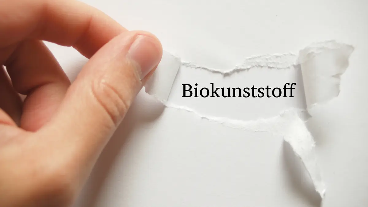 Finger, die ein Papier aufreißen, so dass das Wort Biokunststoff erscheint.