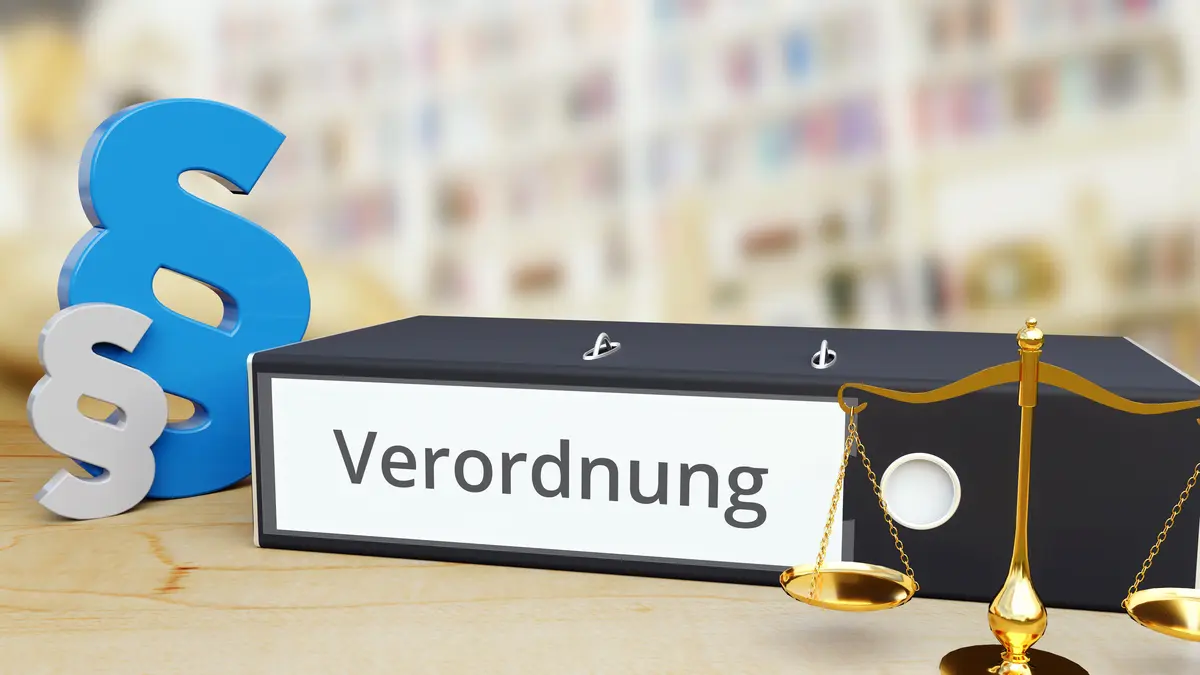 Ein Ordner mit der Aufschrift Verordnung neben einer Waage und dem Paragraphenzeichen.