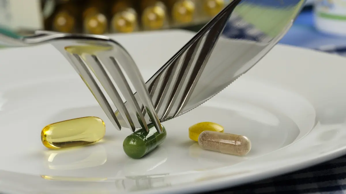 Jemand zerschneidet Schlankheits-Tabletten mit Messer und Gabel auf einem Teller
