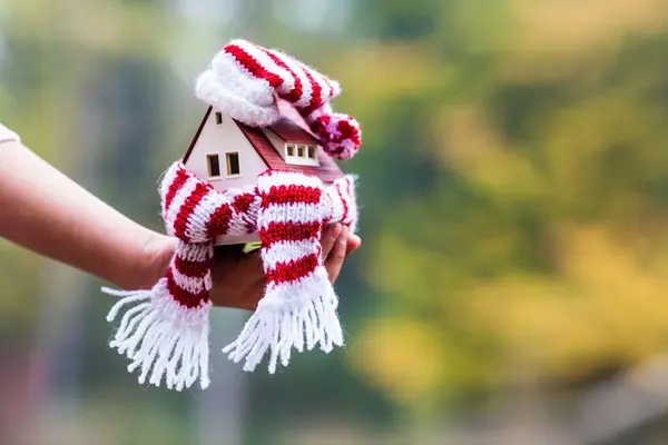 Ein kleines Haus mit einem Schal umwickelt auf einer Hand.
