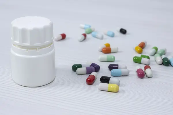 Tablettenkapseln liegen auf einem Tisch, daneben eine geschlossene Pillendose