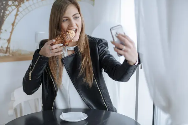 Ein Influencerin filmt sich, wie sie ein Croissant isst