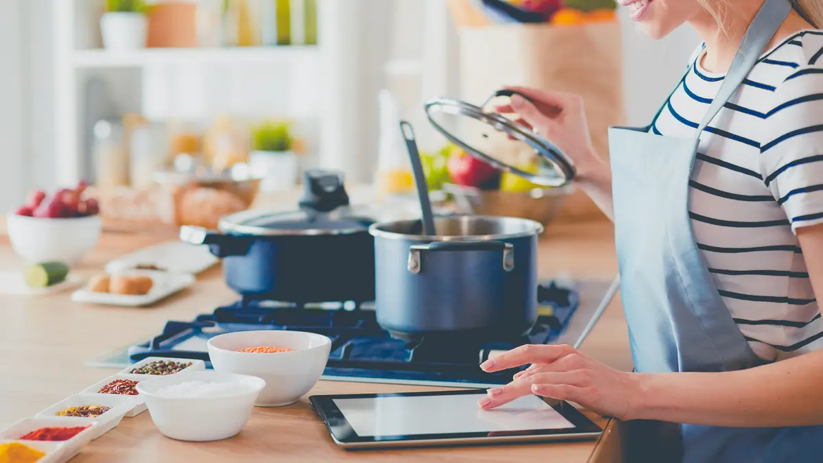 Junge Frau benutzt einen Tablet-Computer zum Kochen in ihrer Küche