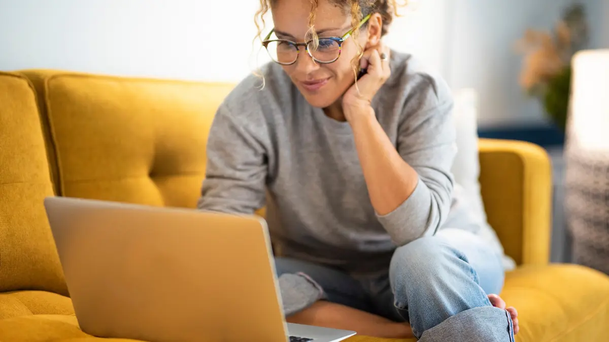 Eine Frau sitzt mit ihrem Laptop auf einem Sofa.