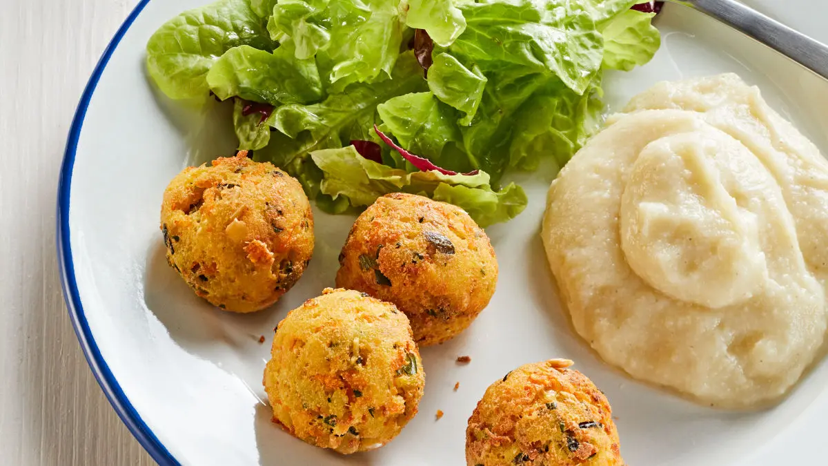 Tofubällchen mit Blumenkohl-Hirse-Püree und Salat auf einem Teller