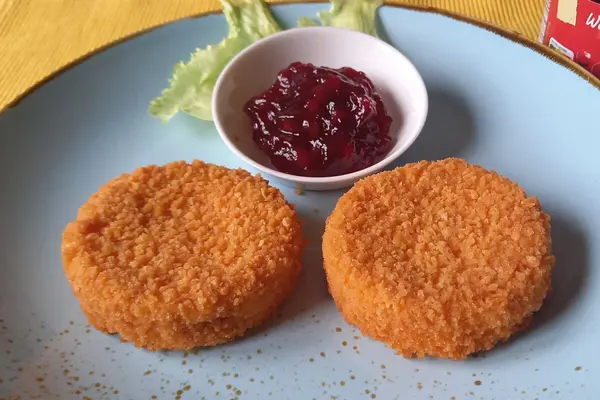 Zwei Scheiben gebackener Camenbert und eine kleine Schüssel mit Preiselbeeren auf einem Teller. 