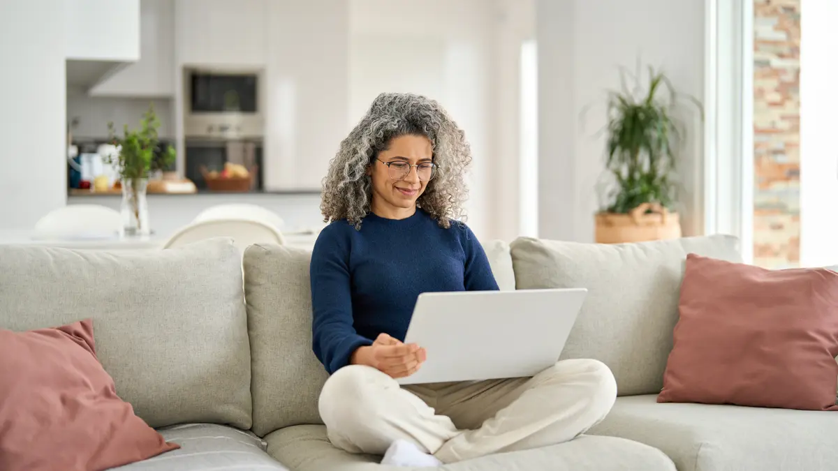 Eine Frau sitzt im Schneidersitz auf einem Sofa mit dem Laptop auf dem Schoß