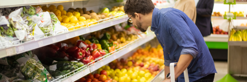 Ein Mann steht gebückt vor dem Gemüseregal und schaut in die Auslage.
