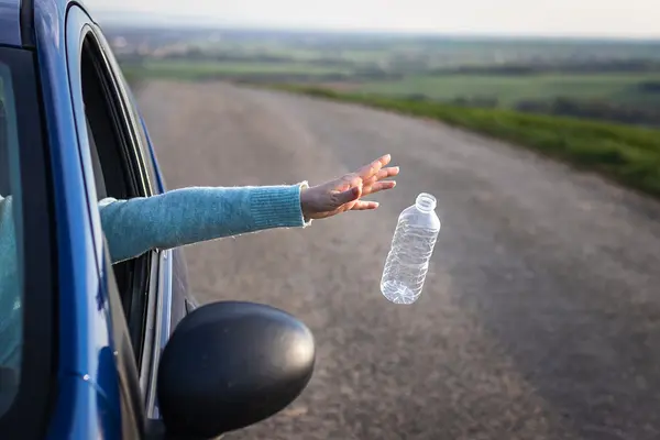 Jemand wirft eine Plastik-Trinkflasche aus dem Autofenster