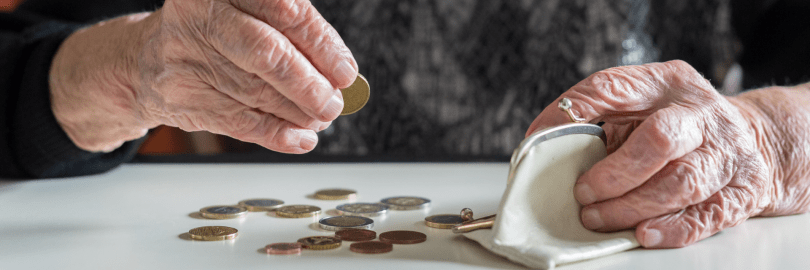 Eine ältere Dame zählt Bargeld, das vor ihr auf dem Tisch liegt