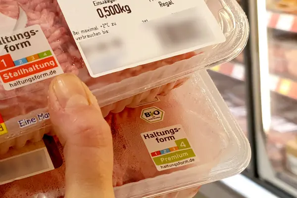Jemand hält zwei Hackfleischpackungen in der Hand, auf denen Haltungs-Logos stehen.