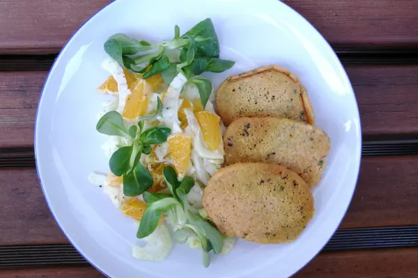 Ein Teller mit Linsenpfannkuchen und Feldsalat mit Orangen