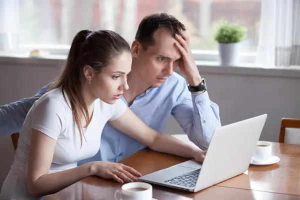 Paar sitzt mit empörtem Gesichtsausdruck vor einem Laptop