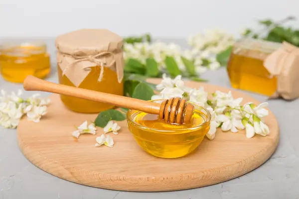 Honigglas, Schüssel mit Honig und Honiglöffel auf Holzbrett, umgeben von Blumen