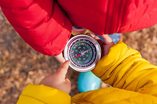 Zwei Kinder in roter und gelber Jacke halten zwischen sich in den Händen einen großen Kompass