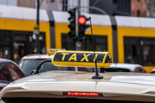 Ein Taxi steht an einer roten Ampel, hinter der eine Straßenbahn abbiegt.